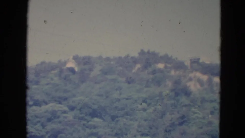 1976 Minnesota 8mm footage shows a hazy tree-covered hillside, with pale forms near the ridge and visible film wear.