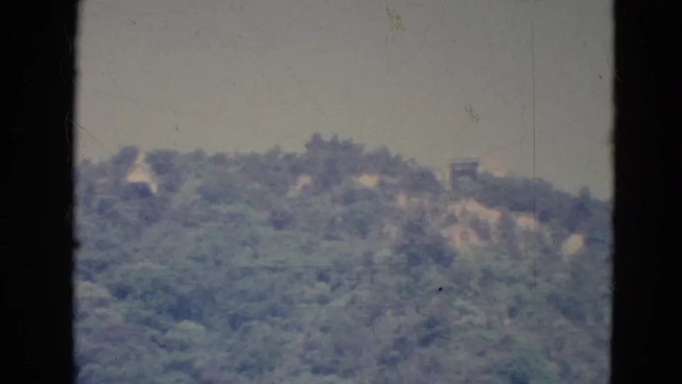 The final 1976 Minnesota frame shows the wooded hillside continuing, with faint pale structures and visible 8mm film wear.