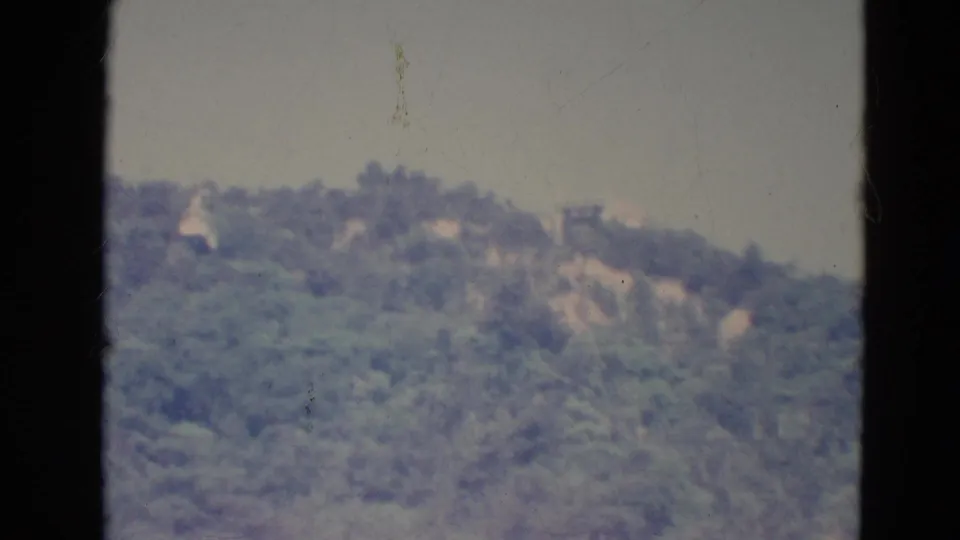 A faded 1976 Minnesota 8mm view of a tree-covered hillside, with dark window framing in the foreground.