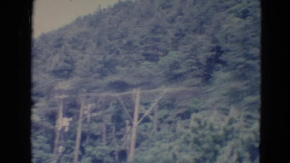 1976 Minnesota 8mm frame showing a wooded hillside with utility poles and wires below the slope.