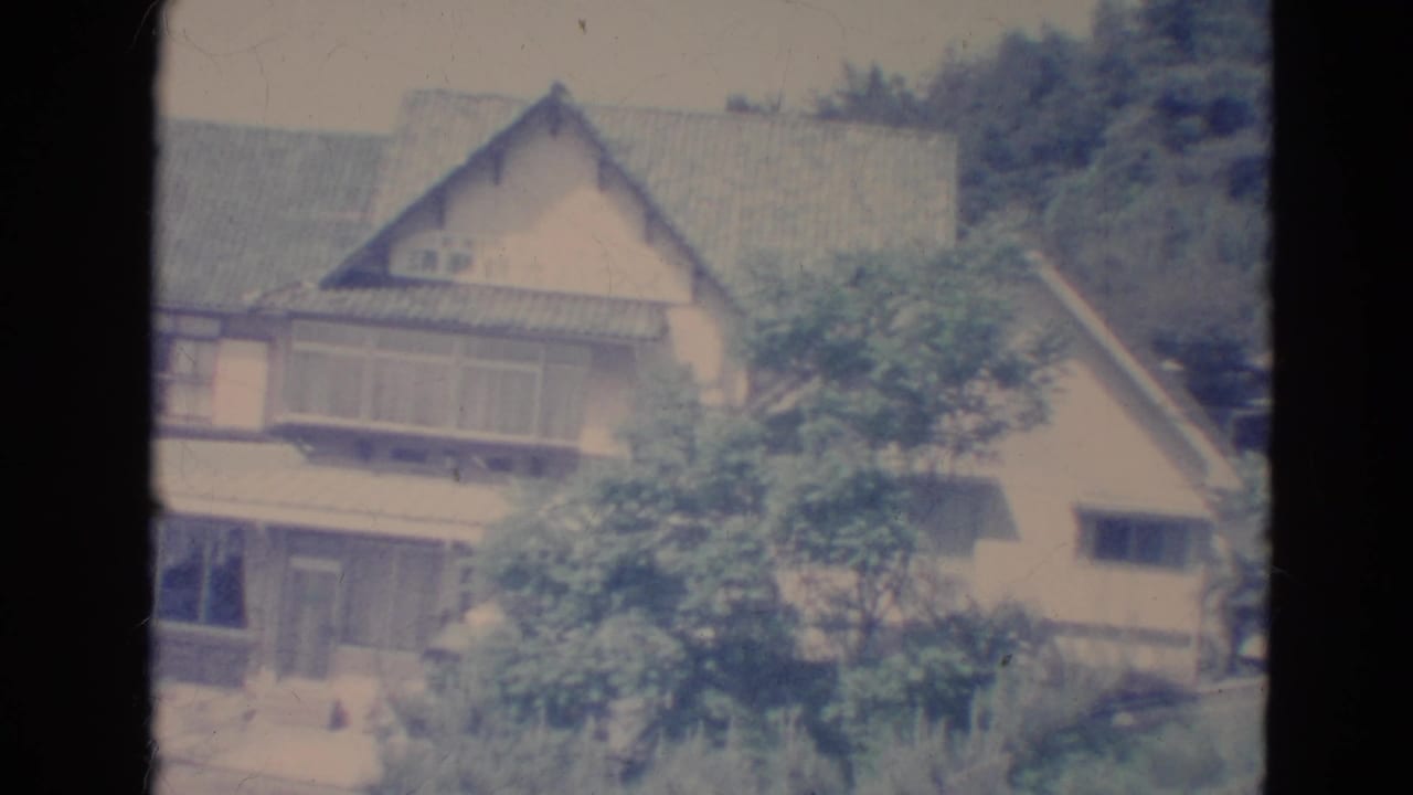 Tan house with roof and trees, framed by dark film borders.