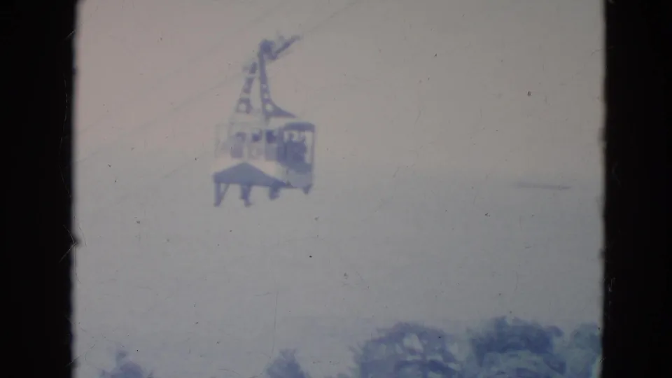 1976 Minnesota 8mm still with a closer skytram cabin, pale sky, blurred treetops, and visible film wear.