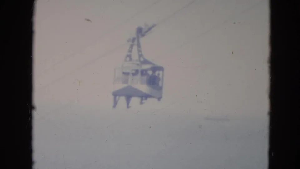1976 Minnesota home-movie still of a skytram cabin centered in a washed-out sky, with possible riders indistinct inside.