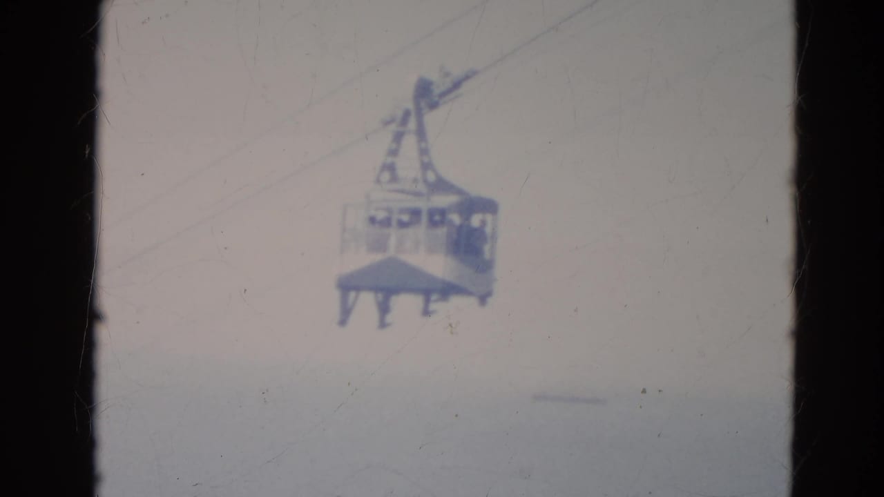 Gondola cable car suspended on overhead cables against a pale sky.