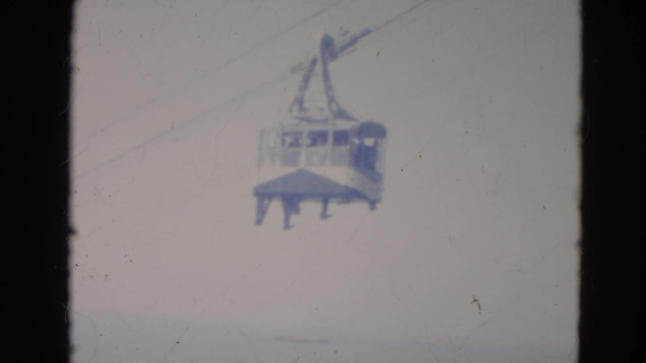 Home-movie frame of a Minnesota gondola cable car suspended in the sky, with indistinct passengers behind the windows.