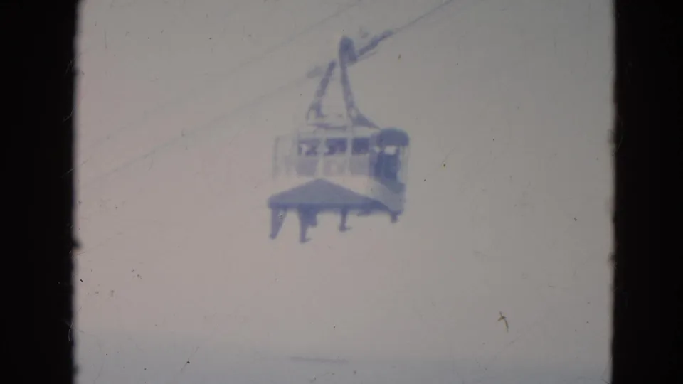 Home-movie frame of a Minnesota gondola cable car suspended in the sky, with indistinct passengers behind the windows.