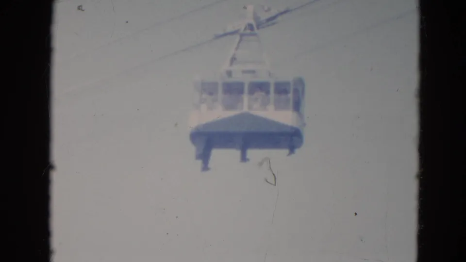 Vintage 8mm frame of a cable car suspended in an overcast Minnesota sky, with indistinct riders inside the cabin.