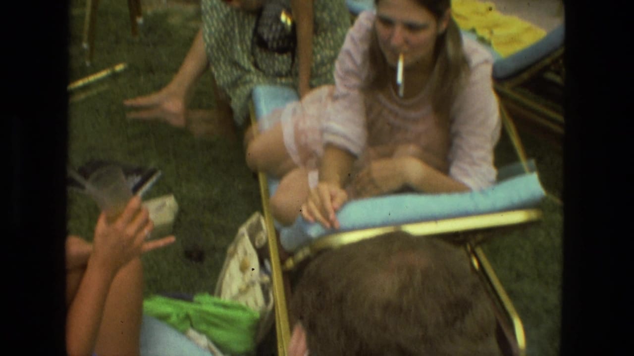 1978 Las Vegas home-movie frame showing adults gathered on grass around blue lounge chairs, including a woman holding a cigarette.