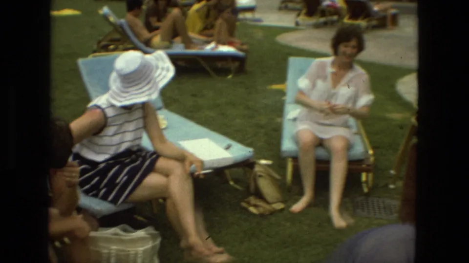 1978 Las Vegas home-movie frame showing a woman in a white sun hat and striped dress seated on a blue lounger among friends.