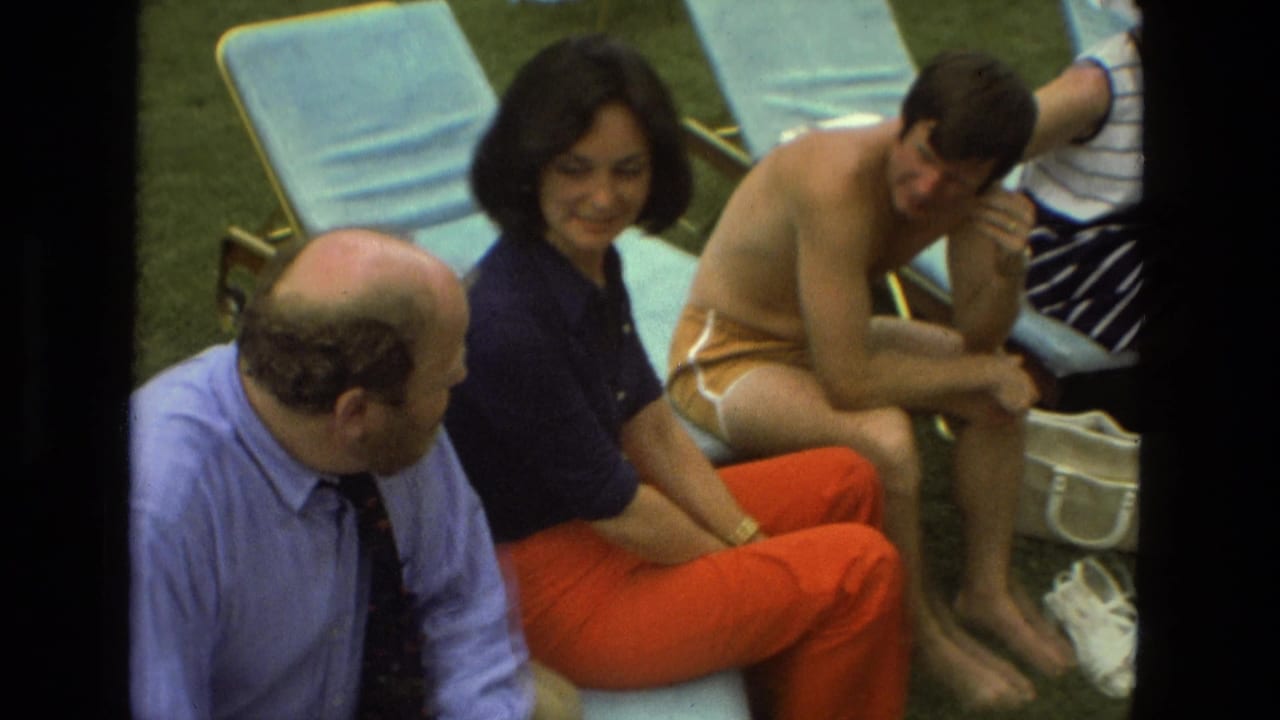 Adults seated on lounge chairs on a lawn, including a woman in orange pants and a man in swim trunks.