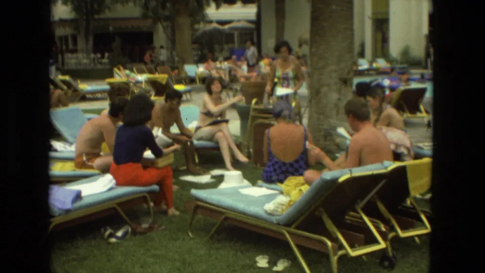 Several adults gather with papers on lounge chairs in a 1978 Las Vegas resort courtyard lined with palms.
