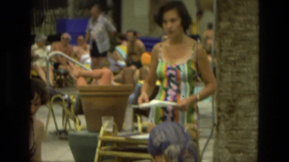 1978 Las Vegas poolside frame with a woman in a bright striped dress holding papers as guests lounge behind her.
