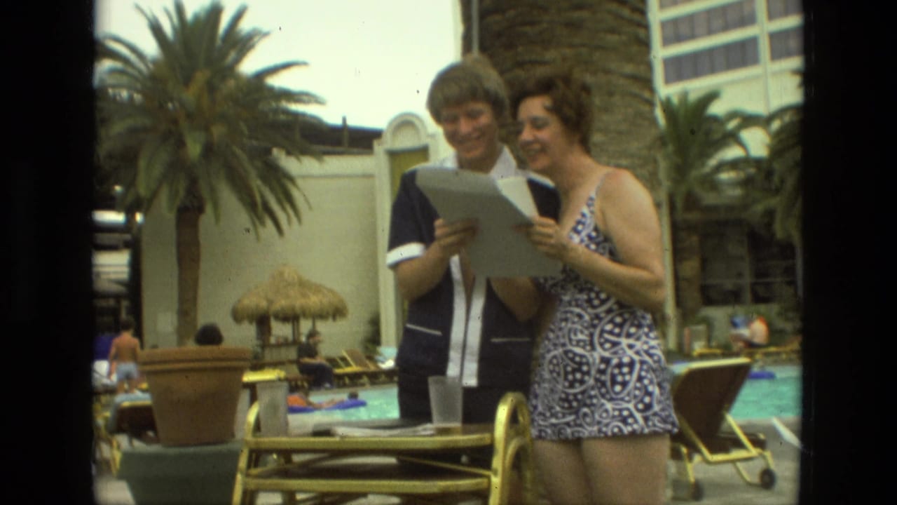Man and woman smile while reading a paper beside a resort pool.
