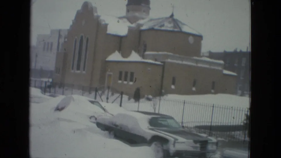 Drexel Hill 1978 frame with parked cars buried in snow beside a church-like building, iron fence, and winter street edge.
