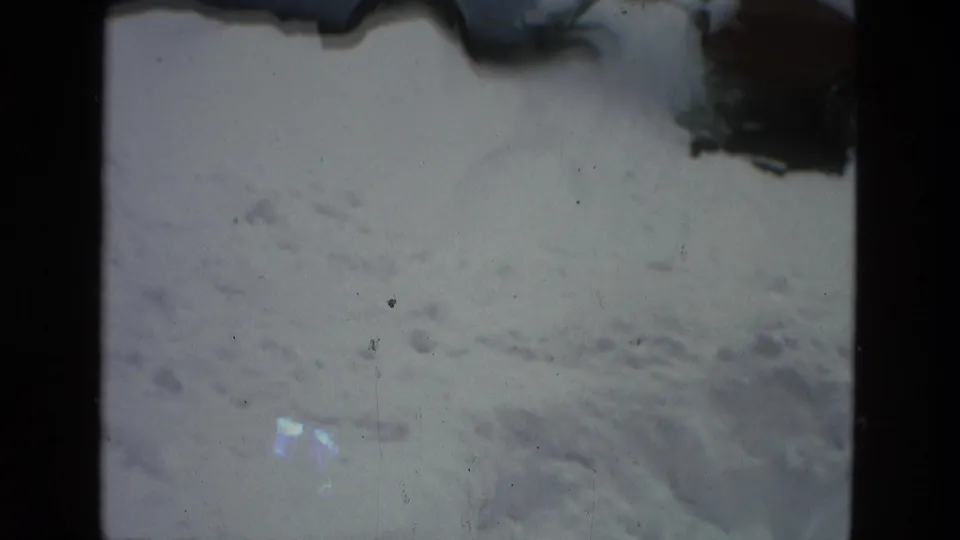 Drexel Hill 1978 home-movie frame looking across deep snow toward partially visible parked cars at the edge of the street.