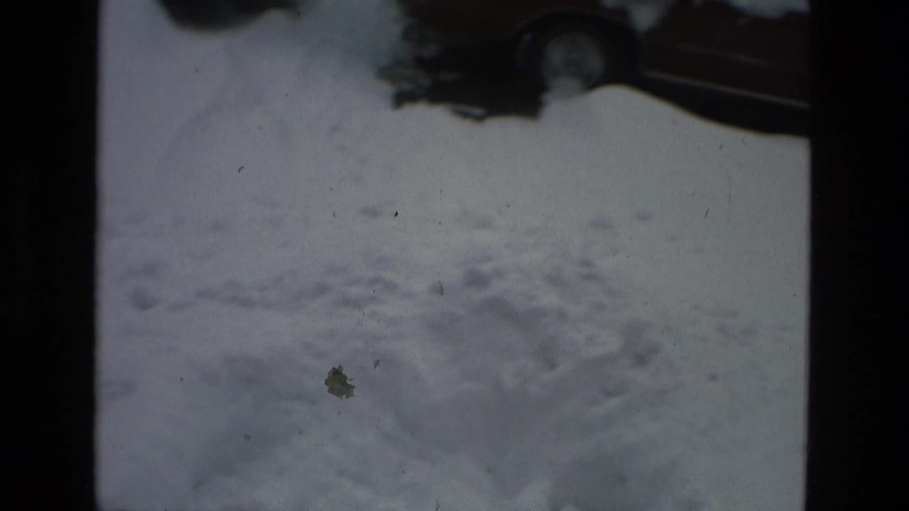 Snow-covered street surface with partial parked cars at the top edge.