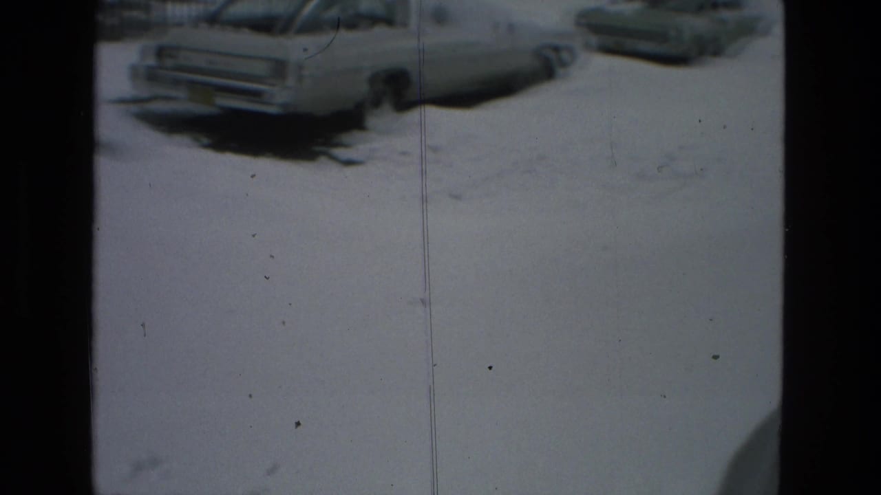 1978 Drexel Hill home-movie frame showing a light-colored car parked along a snow-covered residential street, with another vehicle partly visible nearby.