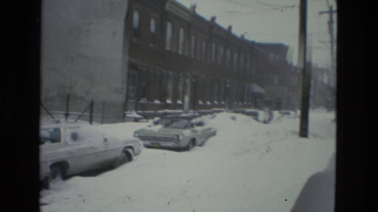 Snow-covered residential street with parked cars, brick townhouses, and utility poles.