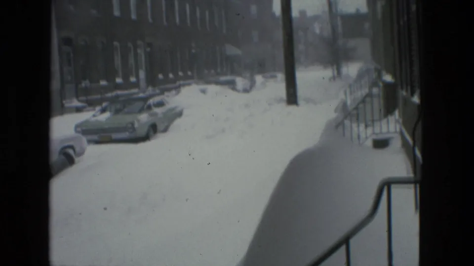 Drexel Hill winter street scene with deep snow against stoop railings, parked cars, brick houses, and a utility pole.