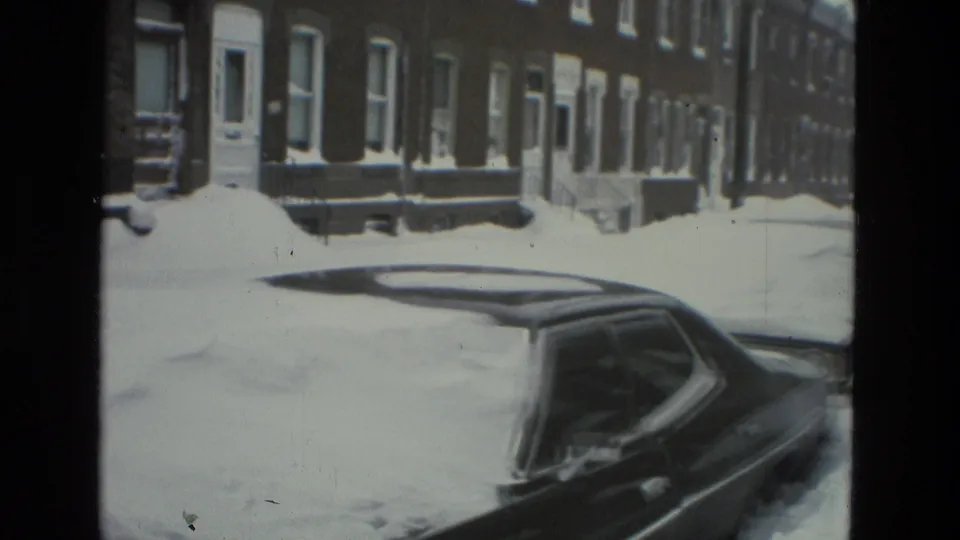 Drexel Hill, Pennsylvania 1978 home-movie frame with a snow-covered car in the foreground and brick houses along the block.