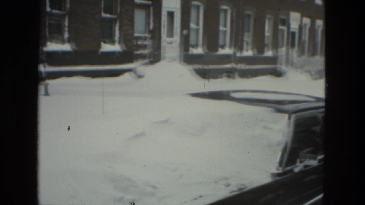 1978 Drexel Hill home-movie frame showing snow blanketing a residential street, row houses, sidewalks, and a parked car.