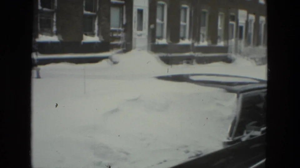 1978 Drexel Hill home-movie frame showing snow blanketing a residential street, row houses, sidewalks, and a parked car.