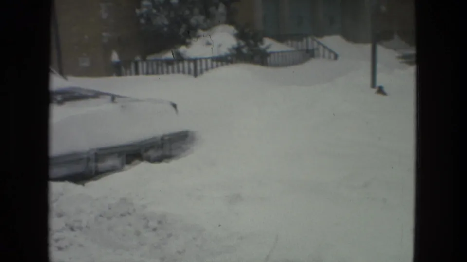 A snow-buried car sits beside railings and residential buildings in Drexel Hill, Pennsylvania, in a 1978 8mm winter scene.
