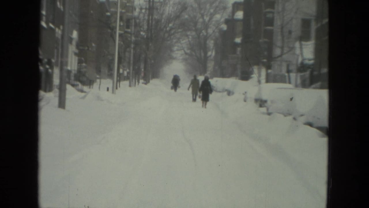 Pedestrians in winter coats walk along a snow-covered Drexel Hill street or sidewalk, with bare trees and buildings nearby.