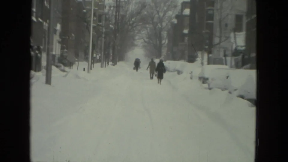 Pedestrians in winter coats walk along a snow-covered Drexel Hill street or sidewalk, with bare trees and buildings nearby.