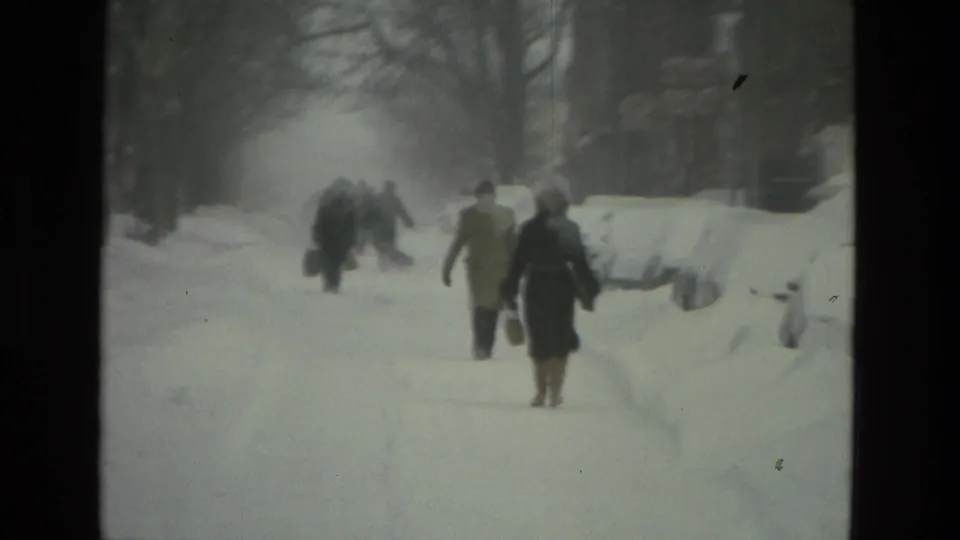 Several people walk through deep snow near parked cars and snowbanks in the 1978 Drexel Hill home-movie footage.