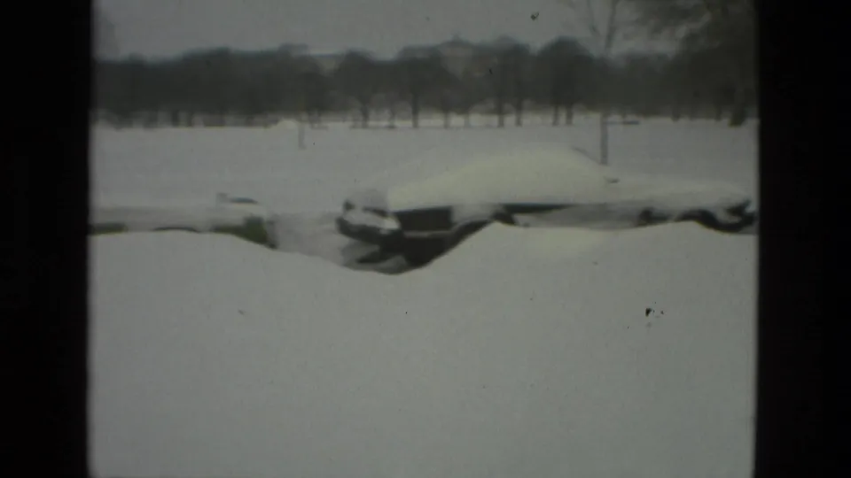 Snow-covered parked cars sit beside an open field or park-like area in Drexel Hill, with bare trees in the background.