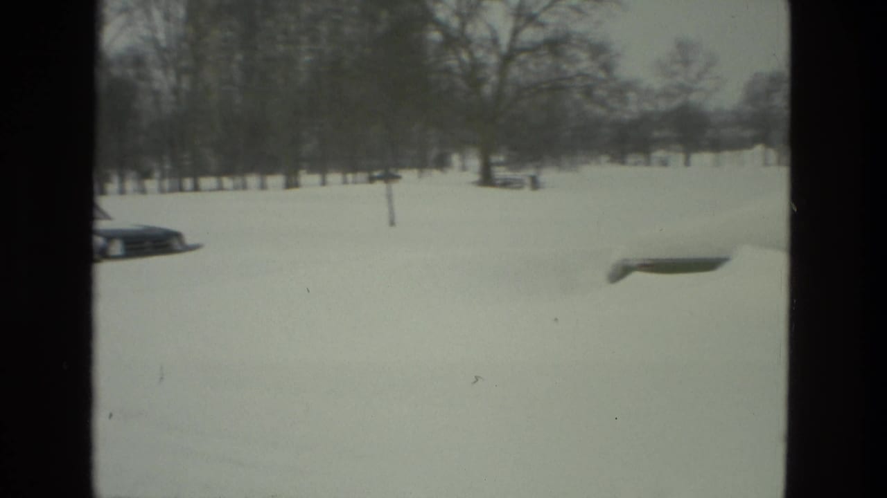 1978 Drexel Hill winter frame with a snowy roadside, parked cars, bare trees, and open residential ground.