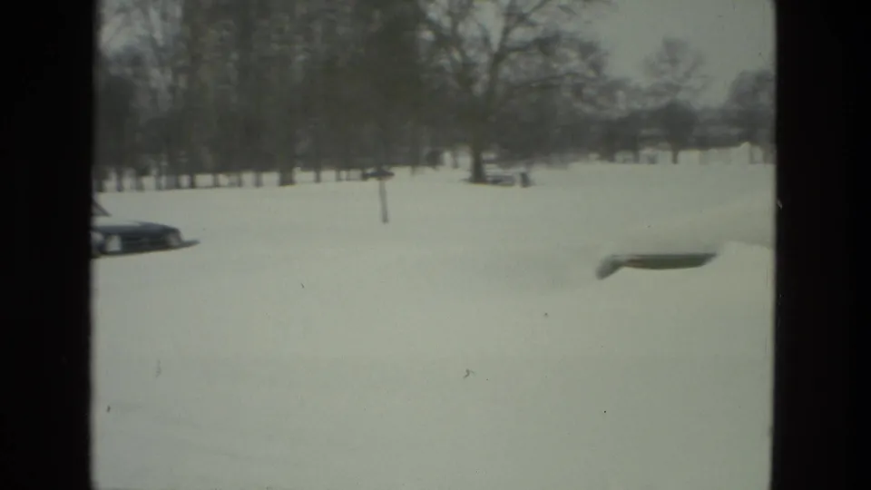 1978 Drexel Hill winter frame with a snowy roadside, parked cars, bare trees, and open residential ground.