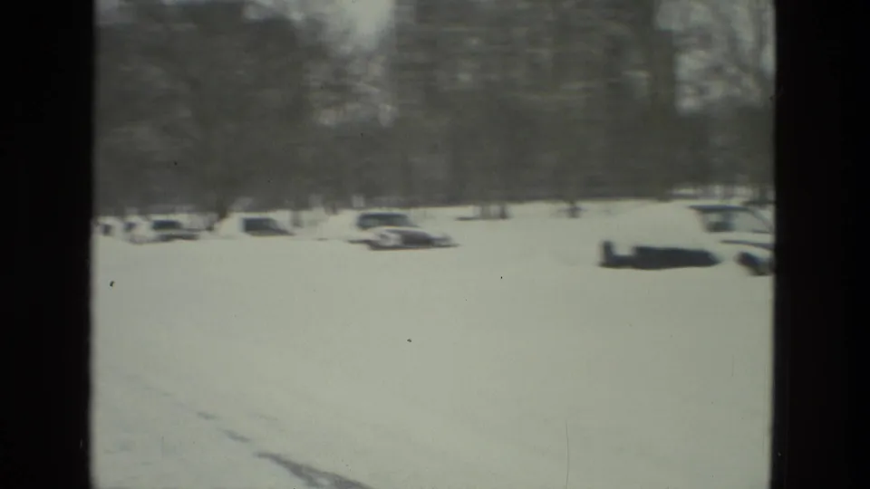 1978 Drexel Hill 8mm frame showing parked cars in deep snow with a distant building softened by focus and film grain.