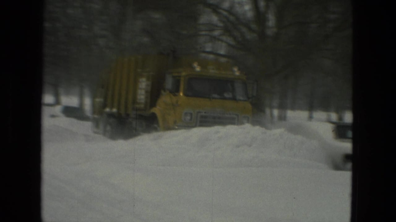 Yellow snowplow truck pushes snow along the right side of a wintry street.