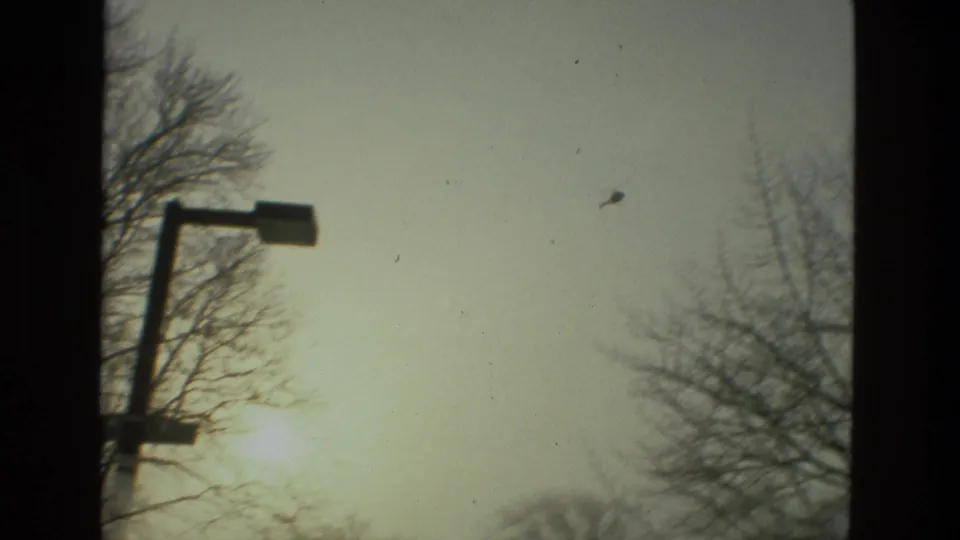 Drexel Hill winter sky in 1978 with a street lamp, bare trees, and a small helicopter passing overhead on 8mm film.
