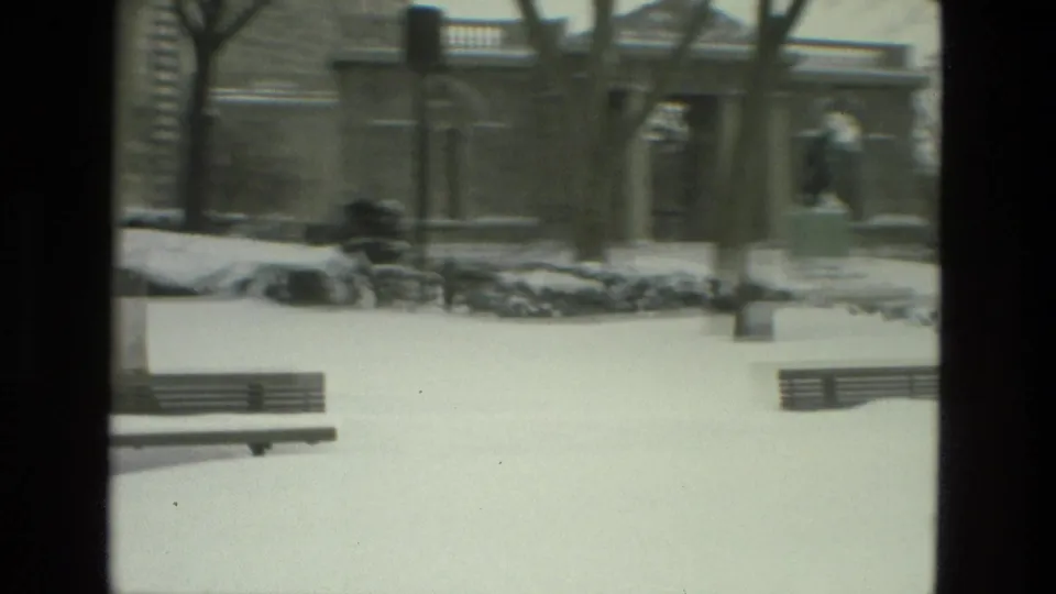 Drexel Hill park in winter, showing benches in snow, leafless trees, a built structure, and a distant statue or sculptural grouping.