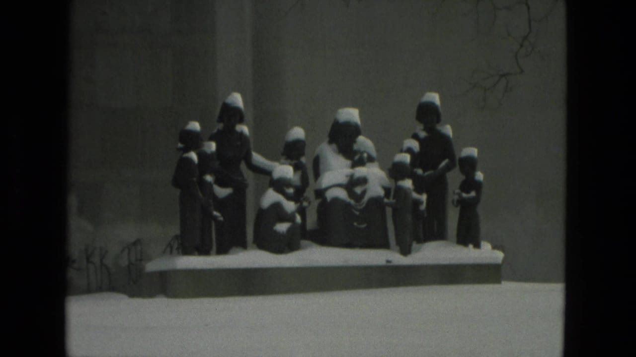 Snow-covered figurative sculpture against a plain wall.