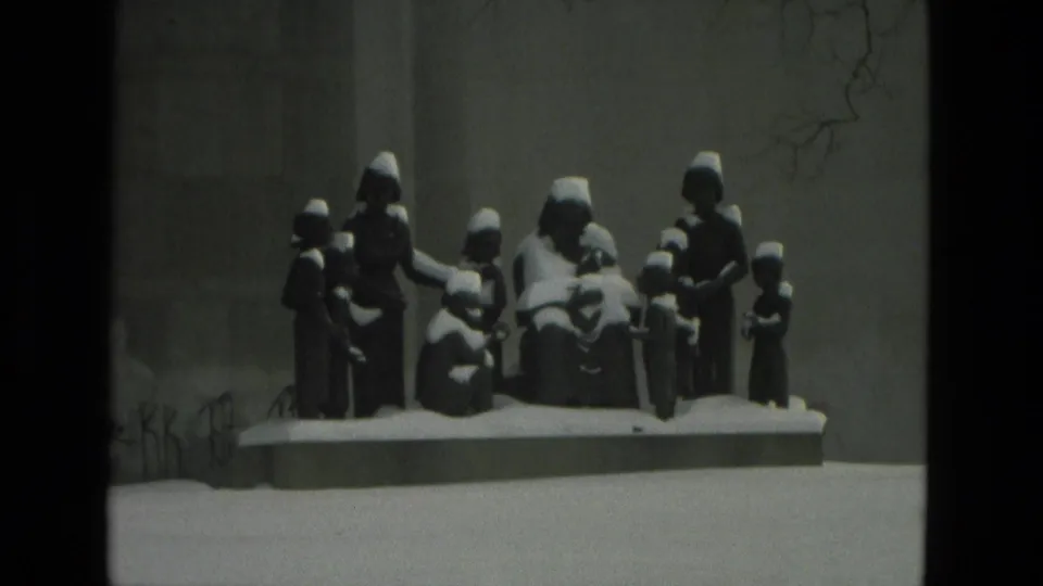 1978 Drexel Hill home-movie frame showing a snow-covered group sculpture on a low plinth near a plain exterior wall.