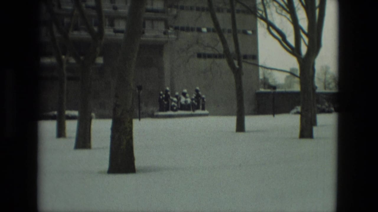 Snowy park grounds with bare trees and a distant sculpture.