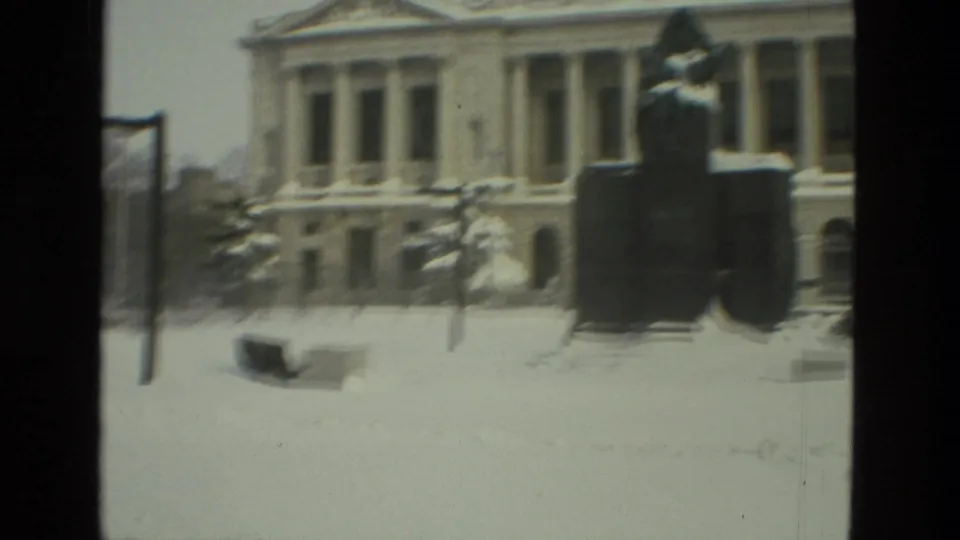 Snowy Drexel Hill frame with a classical columned building behind a dark foreground statue or monument.
