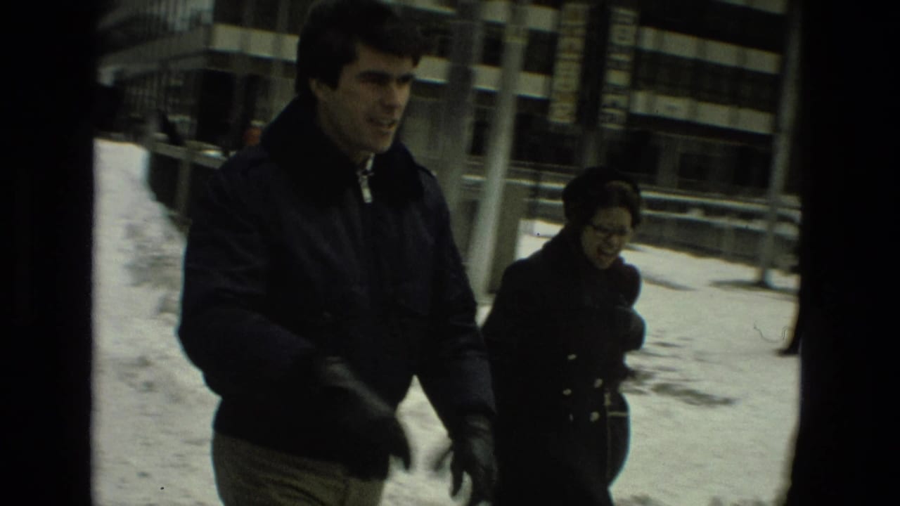 A man and woman in winter clothing walk past snowy sidewalks and urban buildings in the Drexel Hill home-movie footage.