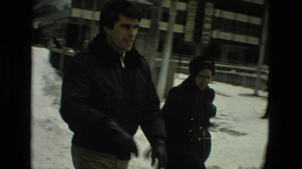 A man and woman in winter clothing walk past snowy sidewalks and urban buildings in the Drexel Hill home-movie footage.