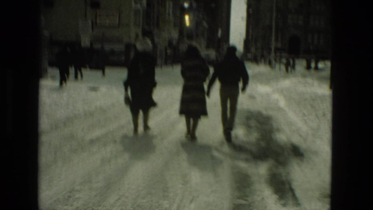 Three people walk away from the camera on a snowy street.