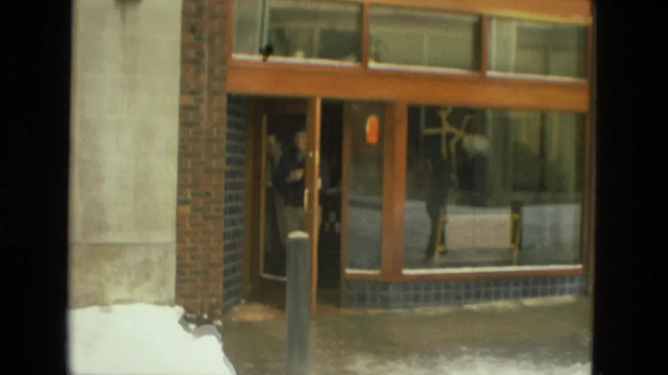 A person appears near the glass entrance of a brick building, with snow piled along the sidewalk in Drexel Hill.
