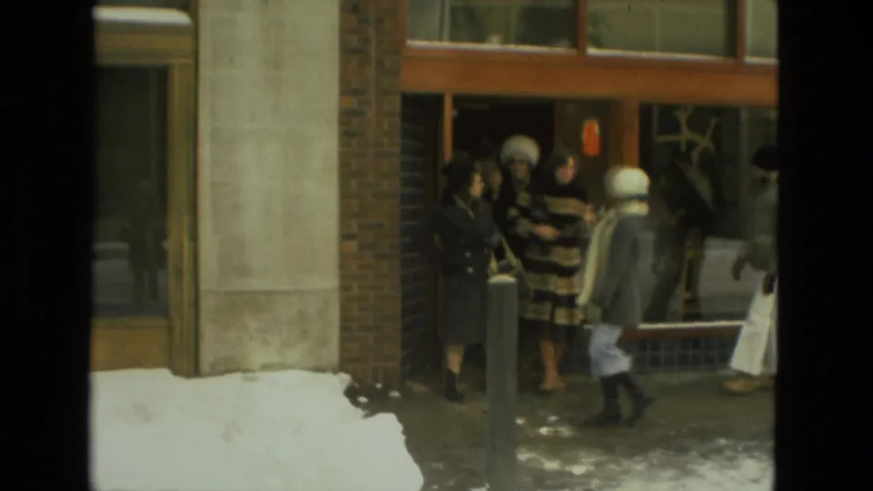 Several people in coats and hats gather at a brick building entrance during a snowy 1978 Drexel Hill street scene.