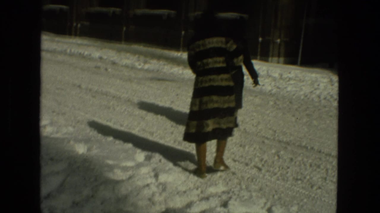 Woman in a striped coat walks through deep snow on a city street.