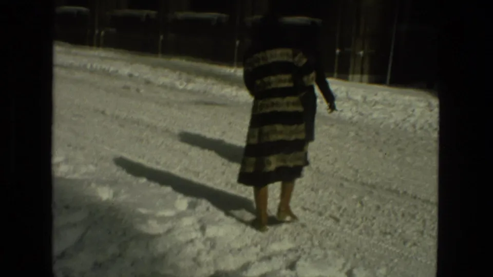 In metadata-supported 1978 Drexel Hill footage, a woman in a black and cream striped coat walks across a snowy street with long shadows.