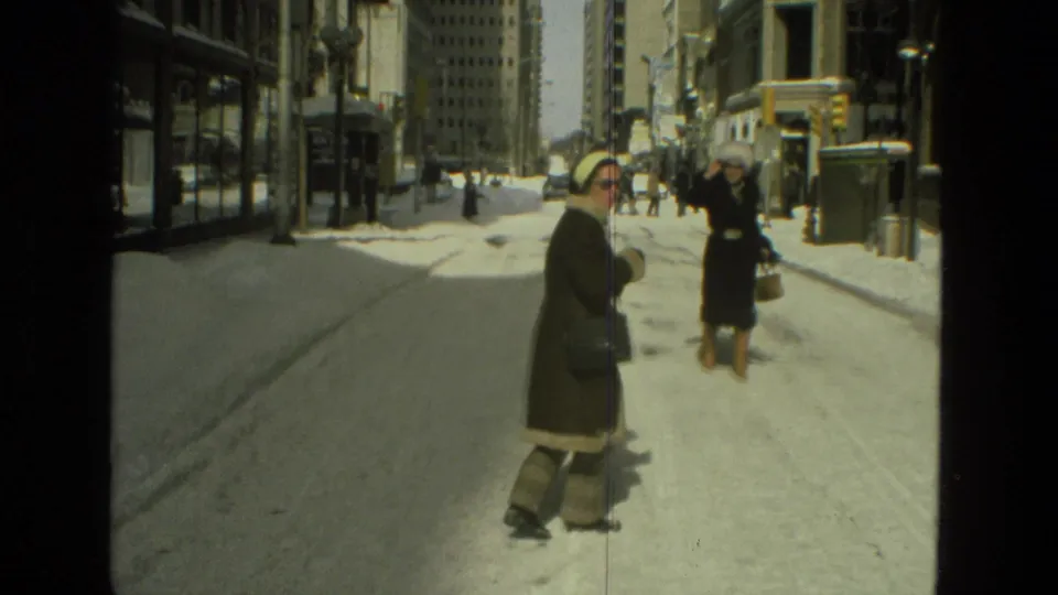 Two bundled women appear on a snow-covered street, with buildings and street fixtures visible in the 1978 Drexel Hill home-movie frame.