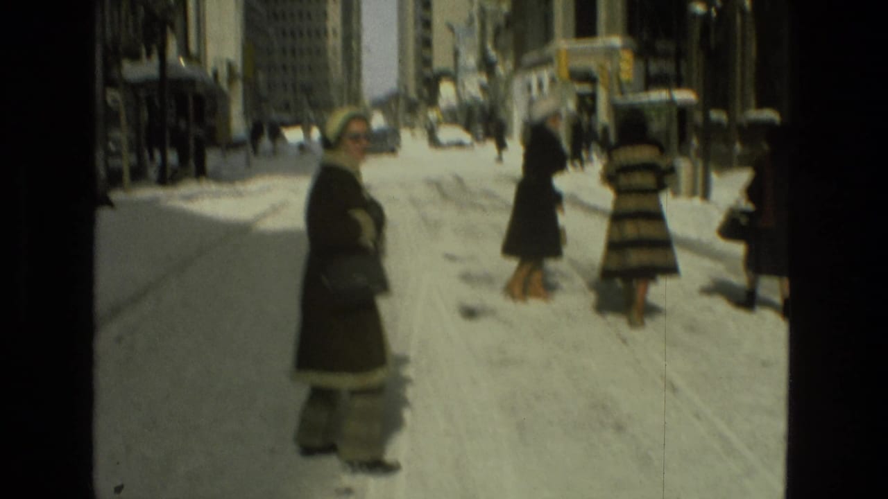 Women in winter coats stand and walk along a snow-covered city street.